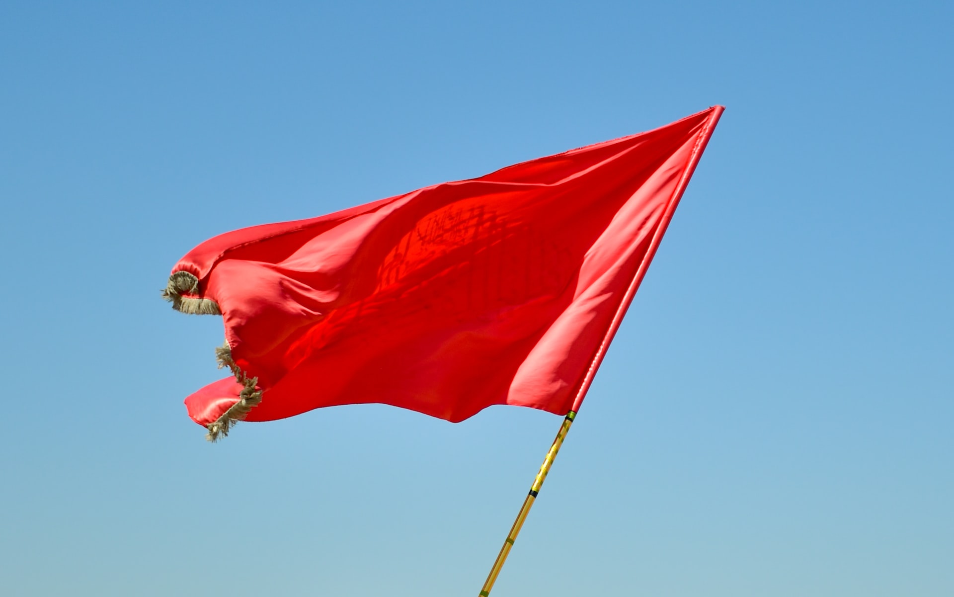 Red flag blows in the wind with blue sky behind, showing idea that writers should be wary of book publisher red flags.