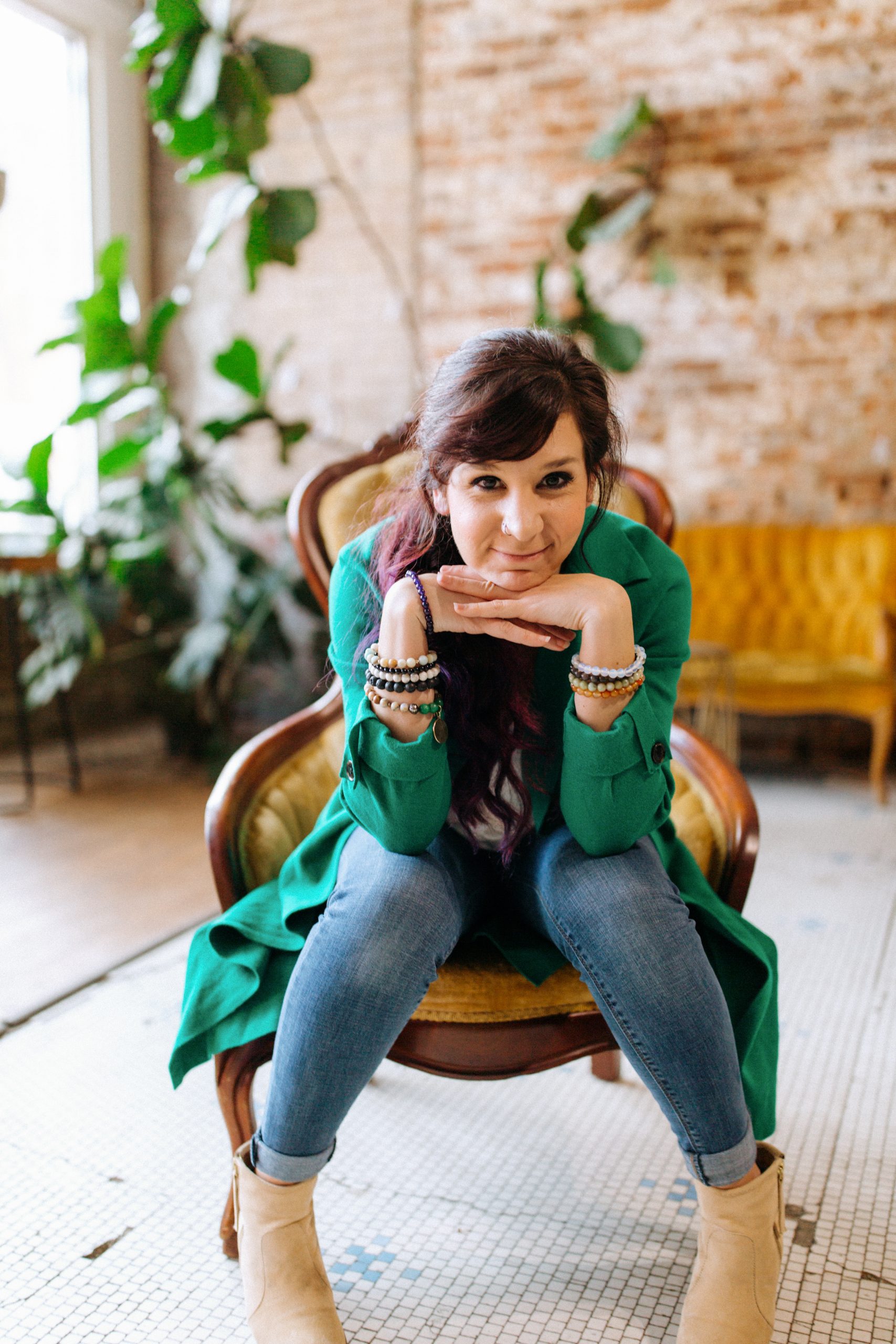 Maverick Malone sits with her hands on her chin. She is wearing a green jacket, black shirt, and blue jeans.