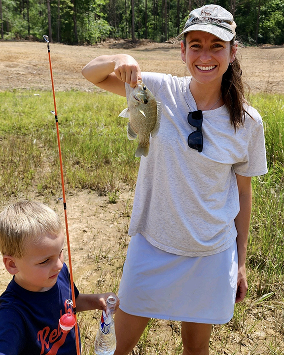 Children's author Betsy Hibbett holding a fish, standing beside her son.