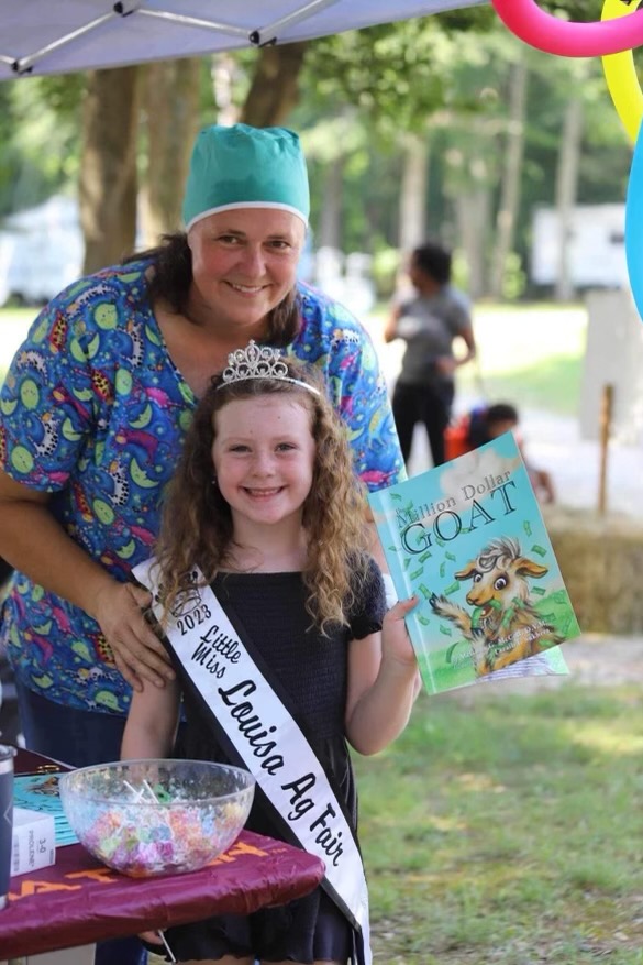 Dr. Melinda McCall stands with Little Miss Louisa County Fair winner, who holds Dr. McCall's new book, The Million Dollar Goat.