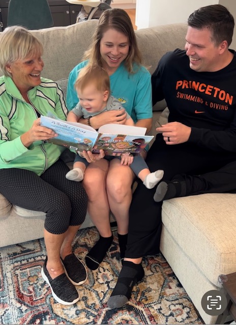 Young Miles, the inspiration for Miles Shares His Smiles, enjoys looking at the picture book with author Nancy Lullo and family
