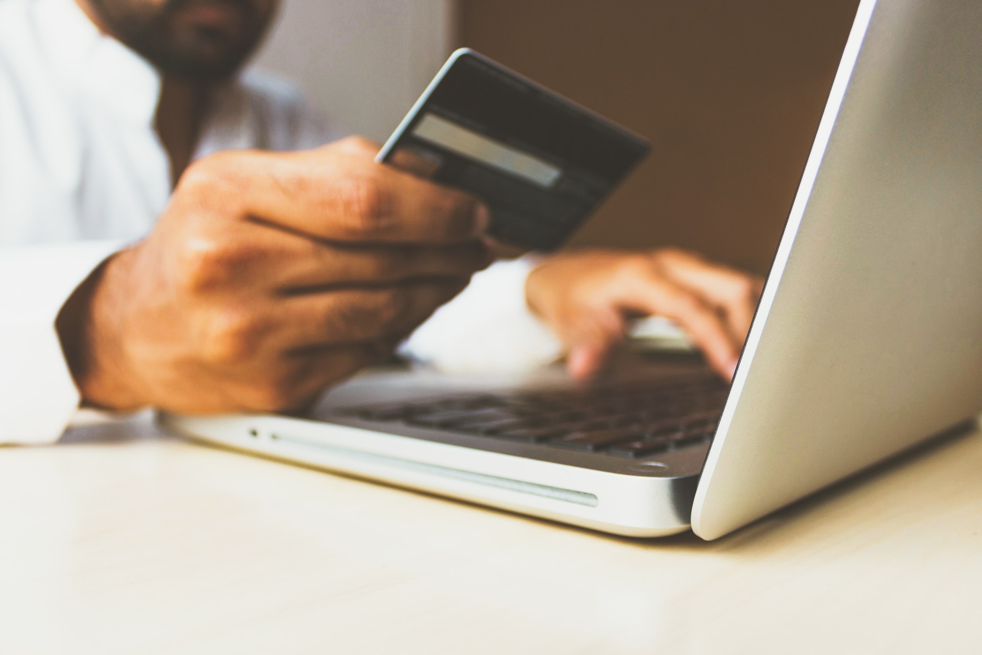 Images shows a man holding a credit card in front of a computer to show that authors can sell their books on their website with IngramSpark Ecommerce