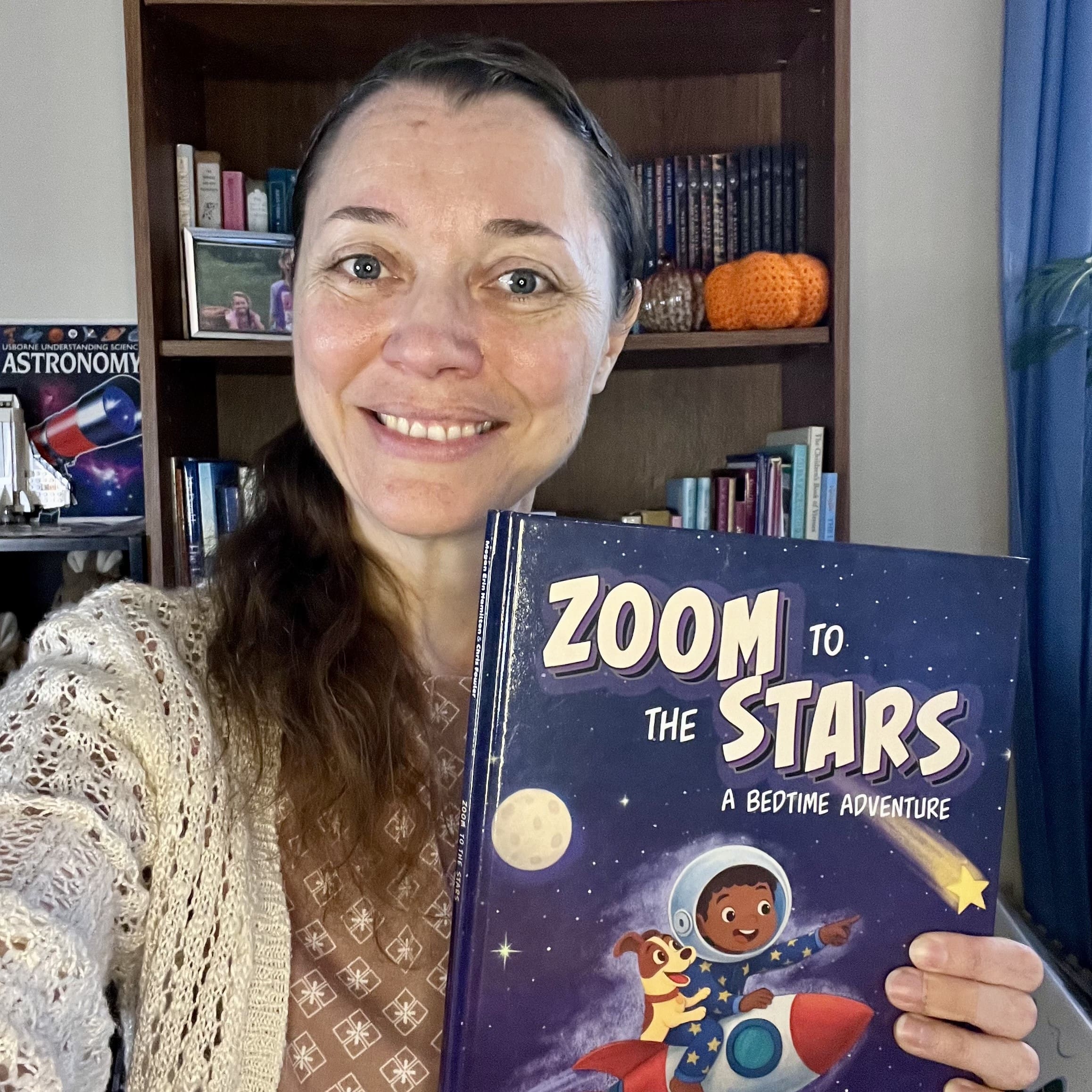 Megan Erin Hamilton smiles and holds her debut picture book, Zoom to the Stars