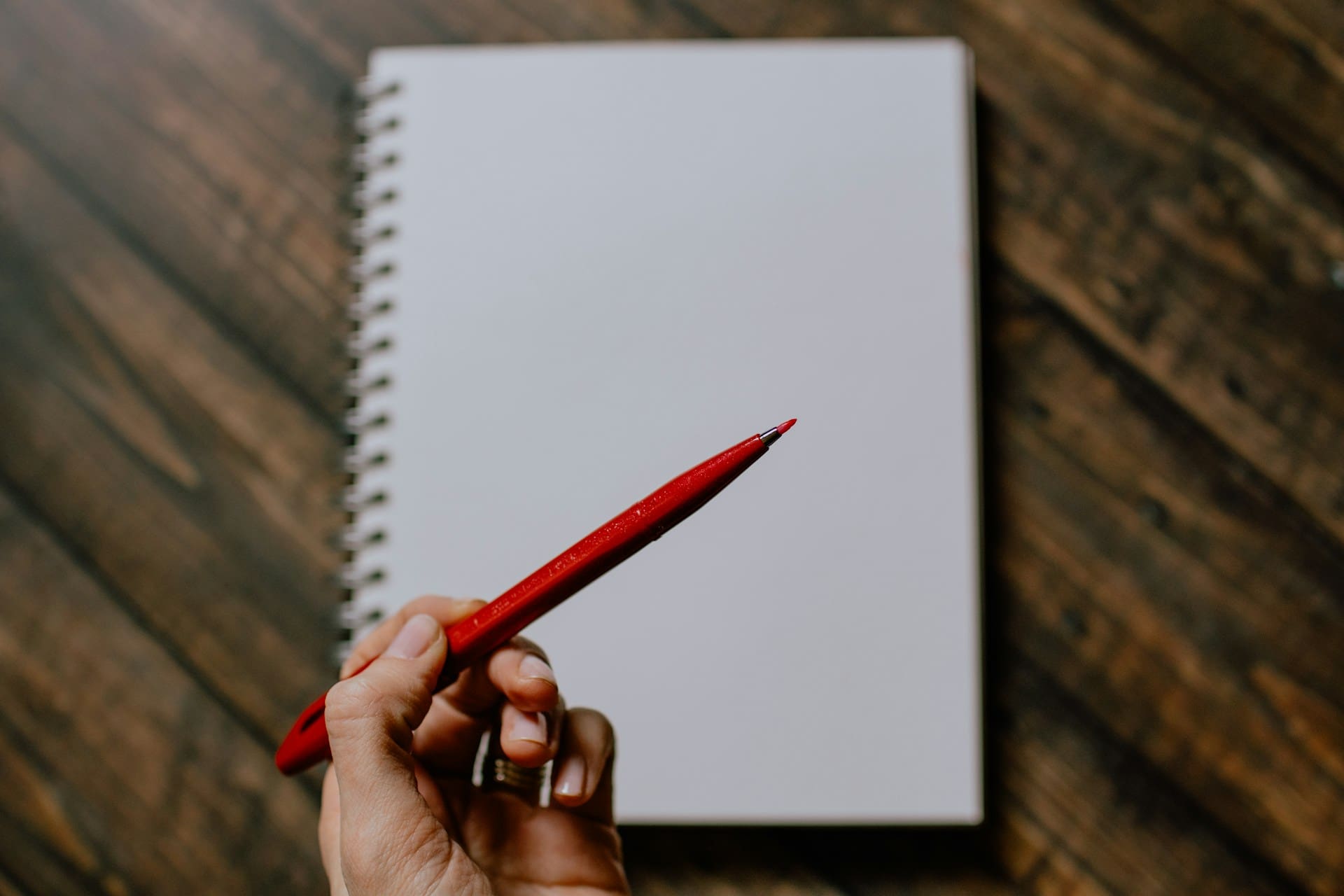 Person holding a red pen over a notebook, illustrating the purpose of the quote - answering the question Does my book really need a professional editor?