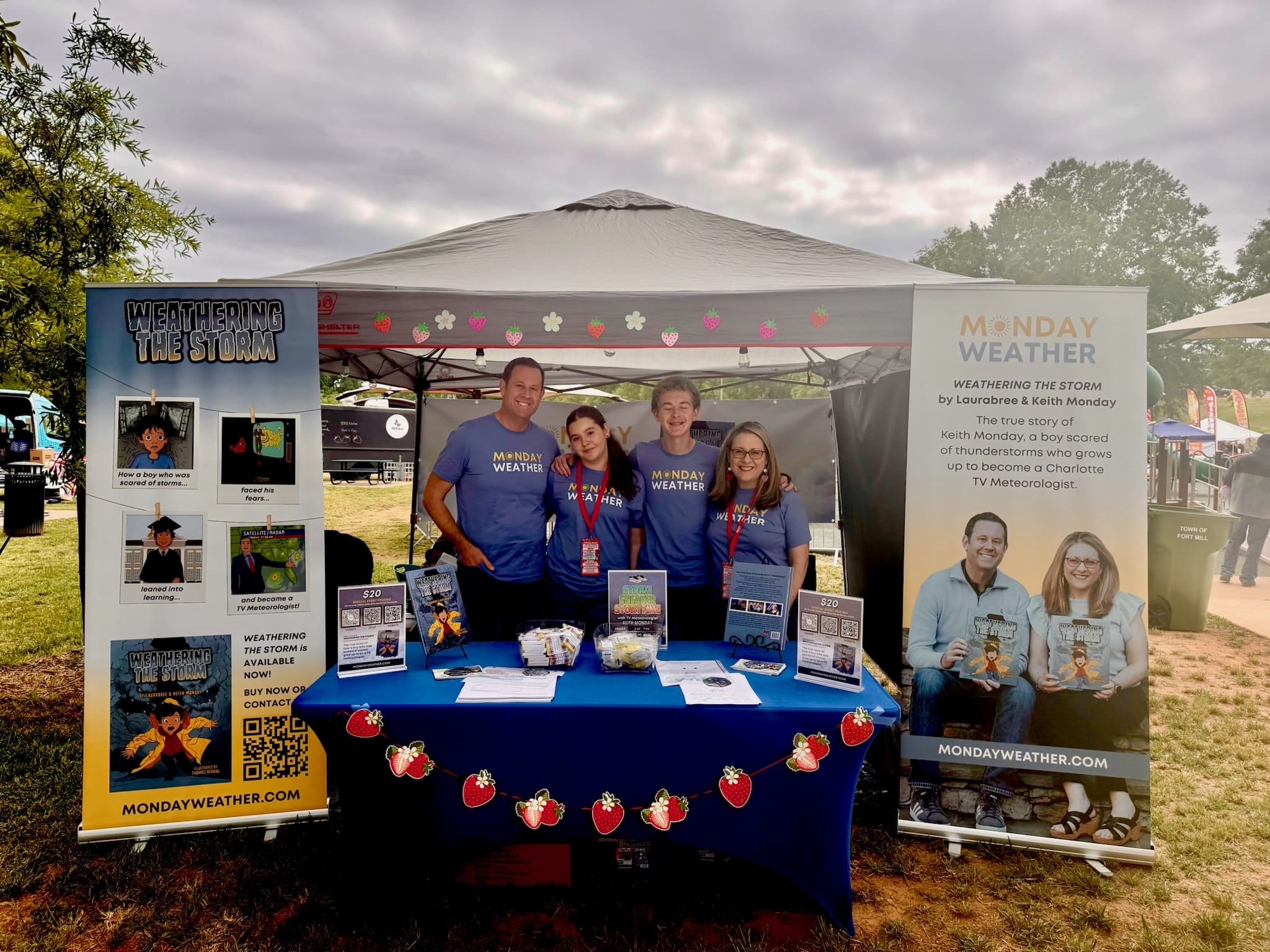 First-time picture book authors Laurabree and Keith Monday with their children under a tent at an event, selling their book, Weathering the Storm.